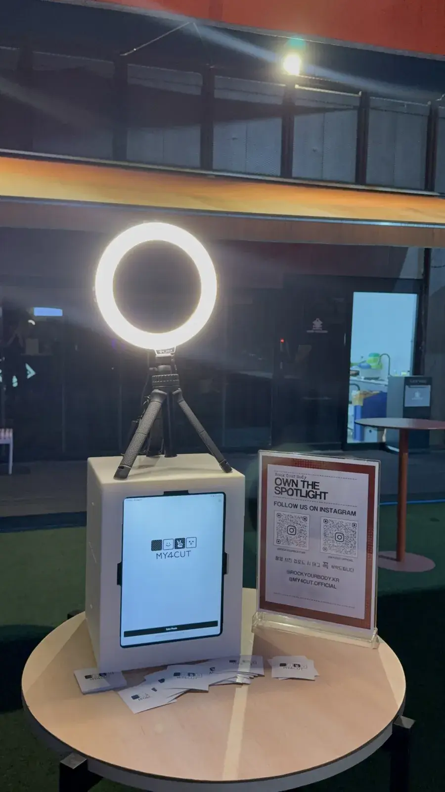 A white mini booth with an iPad on a round rooftop table in Seongsu, a ring light on a tripod above it, a sign beside it