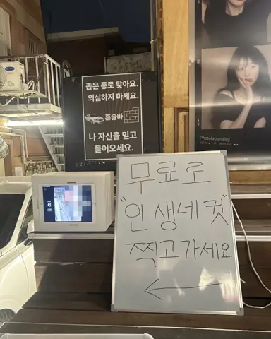 Entrance of DALBAM bar in Haebangchon, a white mini photo booth on the steps under a narrow passage sign and a handwritten whiteboard saying to take a free photo