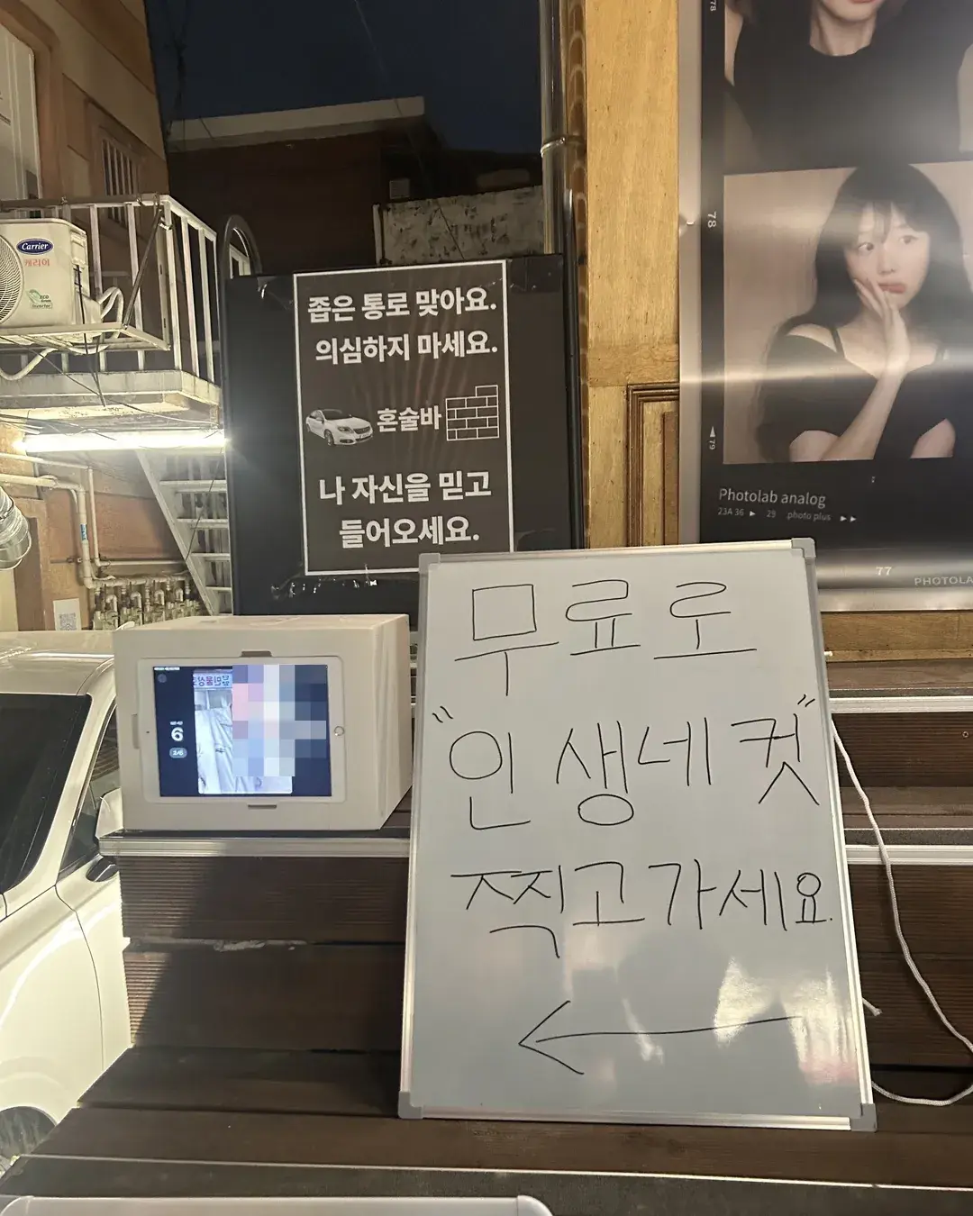 Entrance of DALBAM bar in Haebangchon, a white mini photo booth on the steps under a narrow passage sign and a handwritten whiteboard saying to take a free photo