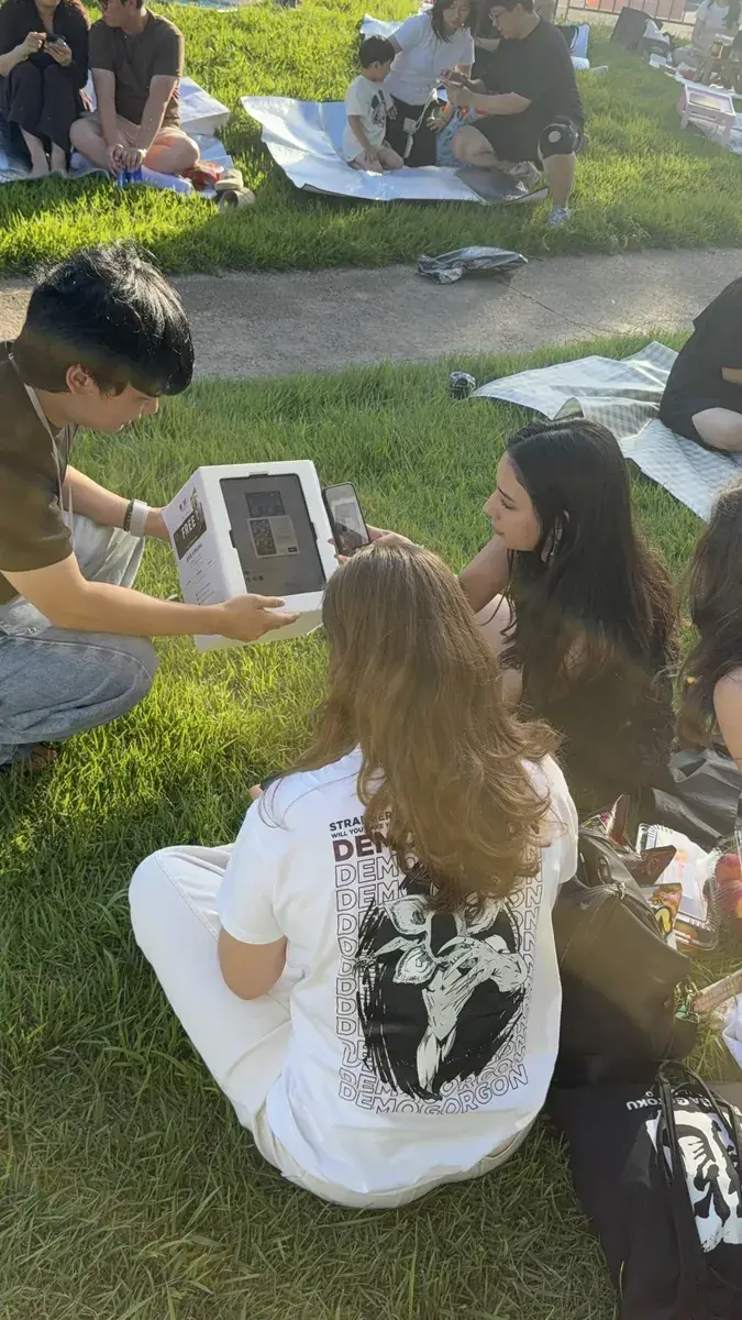 People sitting on picnic blankets at Yeouido Hangang Park taking a photo with a my4cut tablet