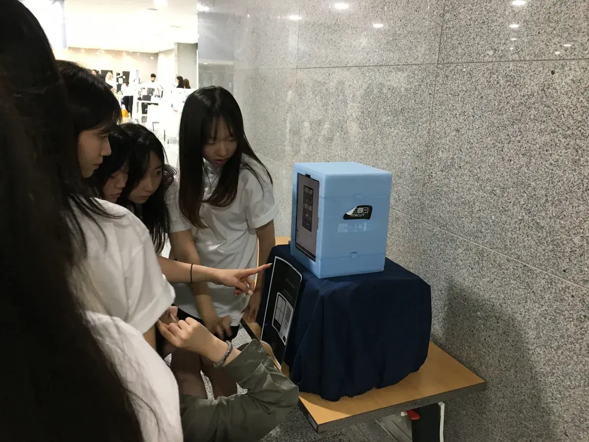 Participants gathered around a my4cut mini photo booth on a table in a demo day lobby