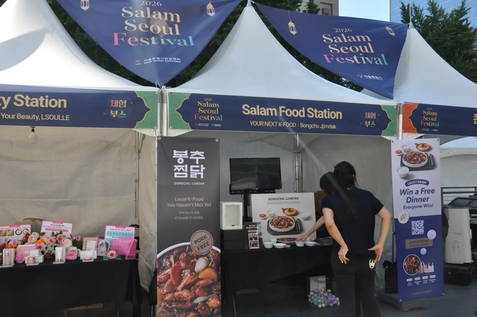 Bongchu Jjimdak promo stall under tents at Salam Seoul Festival, with a monitor, menu board and white mini booth