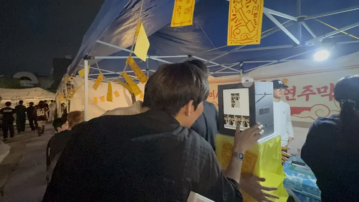 A my4cut mini photo booth on a table under a festival tent at night with students taking photos